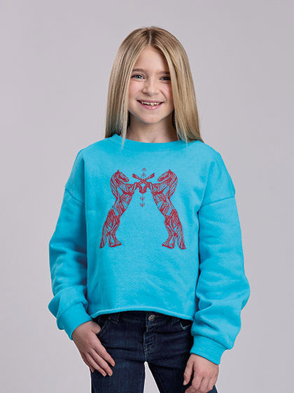 A young girl with blonde hair smiling while wearing a bright turquoise blue sweatshirt with a red graphic of two dancing figures, paired with dark blue jeans, against a solid gray studio background. If you need any assistance with this item or the purchase of this item please call us at five six one seven four eight eight eight zero one Monday through Saturday 10:00a.m EST to 8:00 p.m EST