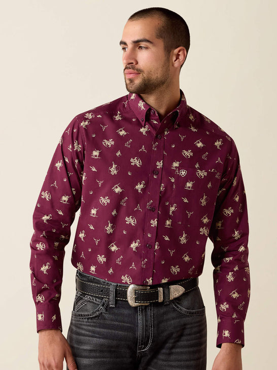 A man wearing a long-sleeve button-down shirt in burgundy with a beige and white cowboy motif, paired with dark gray jeans and a silver belt, against a solid light beige background. If you need any assistance with this item or the purchase of this item please call us at five six one seven four eight eight eight zero one Monday through Saturday 10:00a.m EST to 8:00 p.m EST