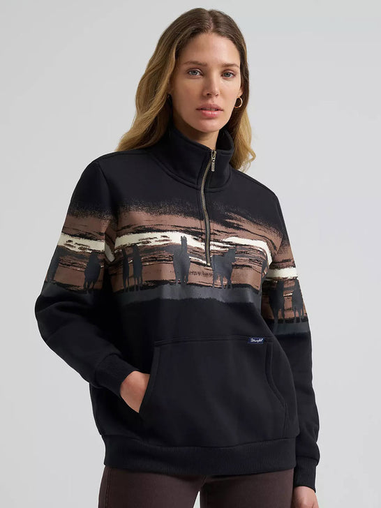 A woman wearing a black quarter-zip sweatshirt with a brown and beige landscape graphic across the chest and upper sleeves, posed against a light gray studio background. If you need any assistance with this item or the purchase of this item please call us at five six one seven four eight eight eight zero one Monday through Saturday 10:00a.m EST to 8:00 p.m EST