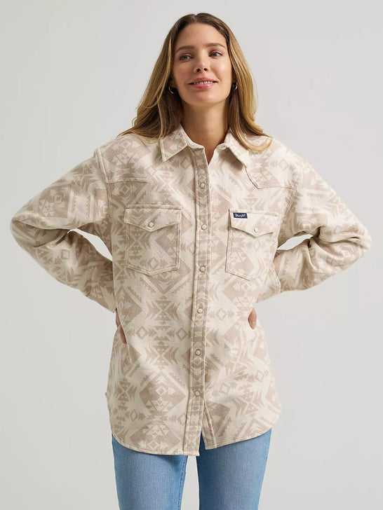 A woman modeling a light beige long-sleeve button-up shirt with a brown geometric southwestern pattern, paired with blue jeans, against a solid light gray background. If you need any assistance with this item or the purchase of this item please call us at five six one seven four eight eight eight zero one Monday through Saturday 10:00a.m EST to 8:00 p.m EST