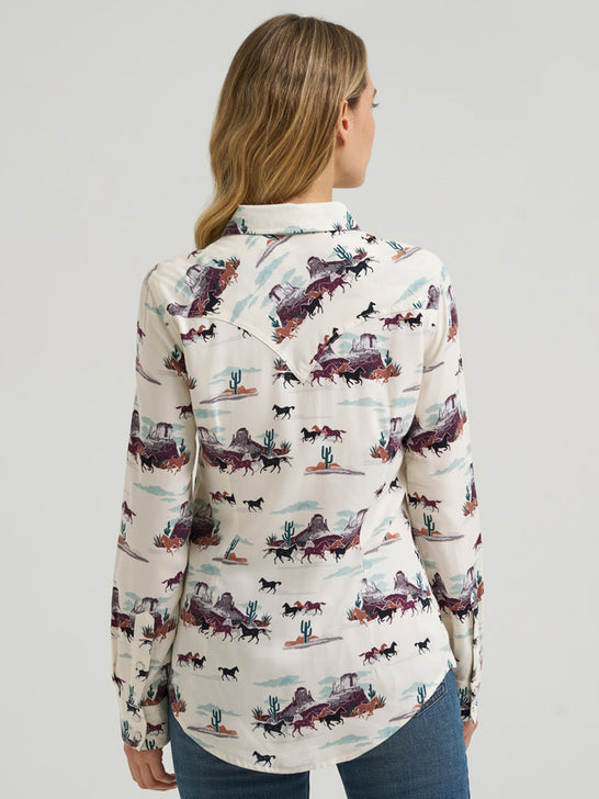A woman shown from the back wearing a long-sleeve button-up shirt with a detailed western-themed print featuring horses, cars, cacti, and desert landscapes on an off-white background. If you need any assistance with this item or the purchase of this item please call us at five six one seven four eight eight eight zero one Monday through Saturday 10:00a.m EST to 8:00 p.m EST