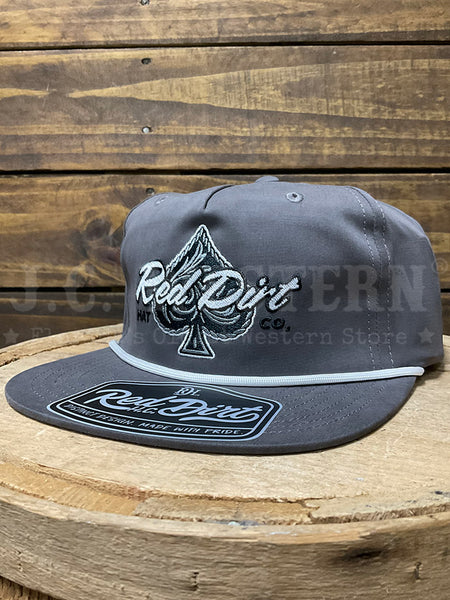 A dark gray snapback cap with a white embroidered spade logo and 'Red Dirt Co.' text on the front, resting on a rustic wooden surface against a wood plank background.If you need any assistance with this item or the purchase of this item please call us at five six one seven four eight eight eight zero one Monday through Saturday 10:00a.m EST to 8:00 p.m EST