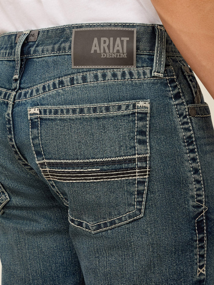 A person wearing dark blue slim-fit jeans with a white t-shirt and black boots, standing against a light beige studio background. If you need any assistance with this item or the purchase of this item please call us at five six one seven four eight eight eight zero one Monday through Saturday 10:00a.m EST to 8:00 p.m EST