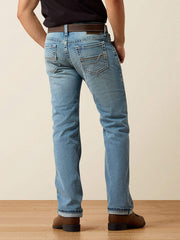 Rear view of a person wearing light blue denim jeans with a brown belt and brown shoes, standing against a plain beige wall on a light wood floor. If you need any assistance with this item or the purchase of this item please call us at five six one seven four eight eight eight zero one Monday through Saturday 10:00a.m EST to 8:00 p.m EST