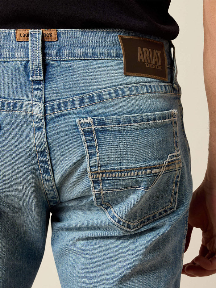 A man wearing light blue straight-leg denim jeans with a brown leather belt, paired with a black t-shirt and brown leather shoes, standing against a neutral beige background. If you need any assistance with this item or the purchase of this item please call us at five six one seven four eight eight eight zero one Monday through Saturday 10:00a.m EST to 8:00 p.m EST