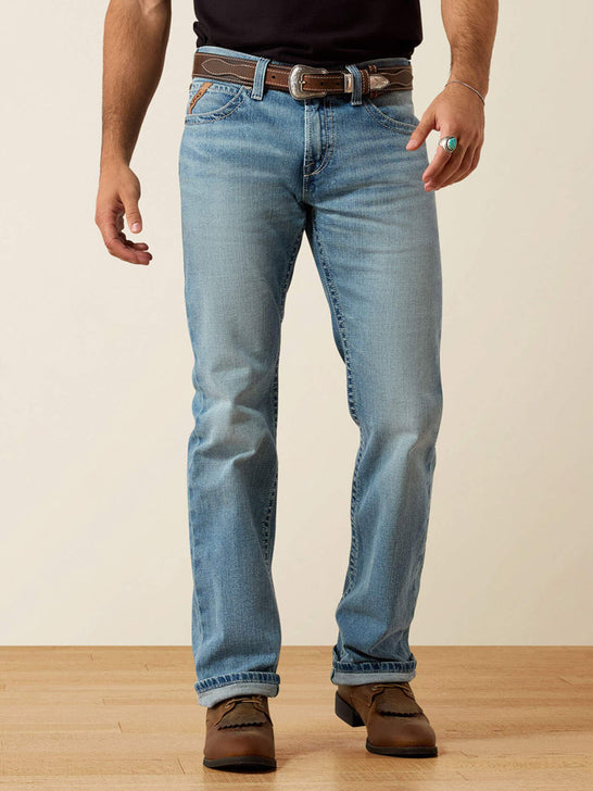 A man wearing light blue straight-leg denim jeans with a brown leather belt, paired with a black t-shirt and brown leather shoes, standing against a neutral beige background. If you need any assistance with this item or the purchase of this item please call us at five six one seven four eight eight eight zero one Monday through Saturday 10:00a.m EST to 8:00 p.m EST