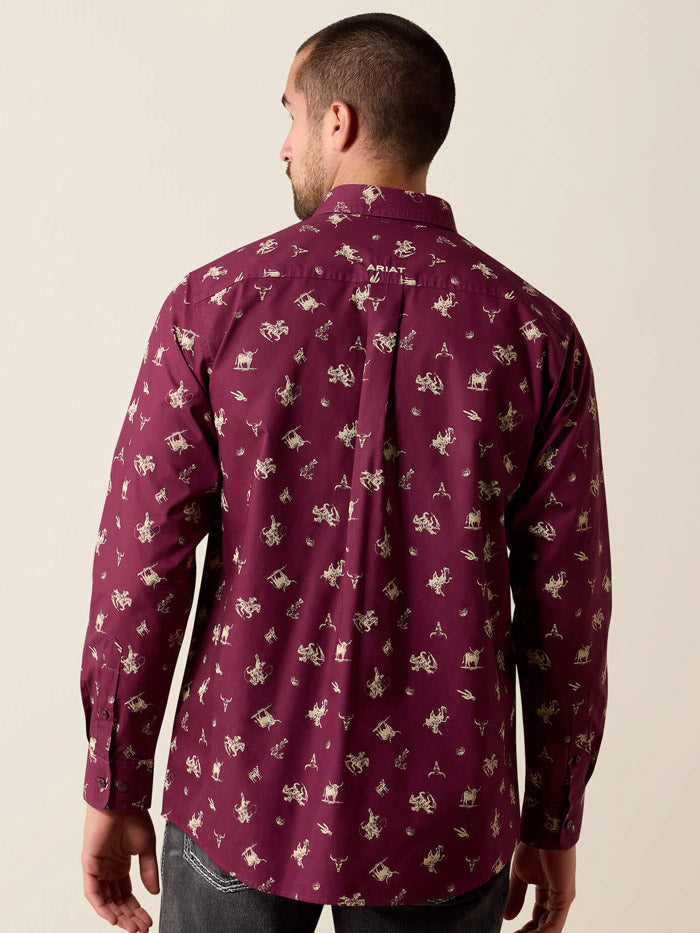 A man wearing a long-sleeve button-down shirt in burgundy with a beige and white cowboy motif, paired with dark gray jeans and a silver belt, against a solid light beige background. If you need any assistance with this item or the purchase of this item please call us at five six one seven four eight eight eight zero one Monday through Saturday 10:00a.m EST to 8:00 p.m EST