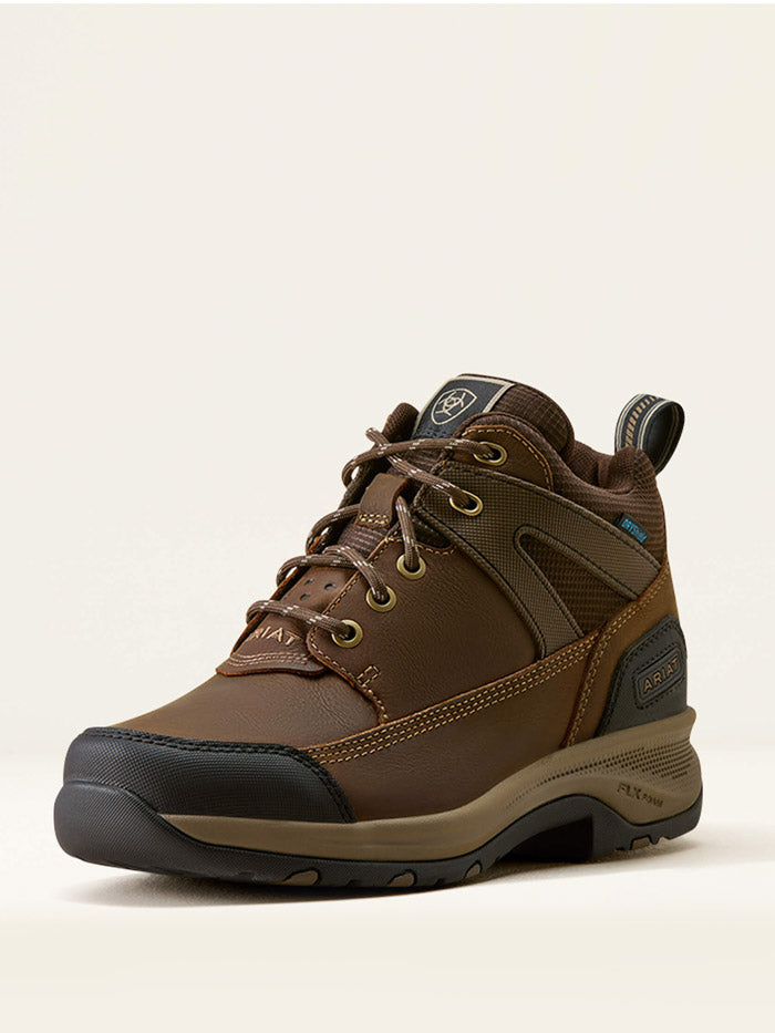 A brown mid-cut hiking boot with a black and tan sole, shown from a three-quarters angle against a light beige background. If you need any assistance with this item or the purchase of this item please call us at five six one seven four eight eight eight zero one Monday through Saturday 10:00a.m EST to 8:00 p.m EST