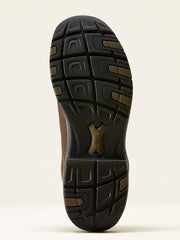 A close-up view of the treaded outsole of a brown boot, showing a black rubber sole with brown lugs and a central metallic gold logo, set against a plain off-white background. If you need any assistance with this item or the purchase of this item please call us at five six one seven four eight eight eight zero one Monday through Saturday 10:00a.m EST to 8:00 p.m EST