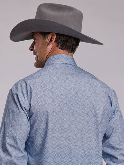 A smiling man wearing a light blue western long-sleeve button-up shirt, dark blue jeans, a black belt, and a gray cowboy hat, photographed against a plain light gray studio background. If you need any assistance with this item or the purchase of this item please call us at five six one seven four eight eight eight zero one Monday through Saturday 10:00a.m EST to 8:00 p.m EST