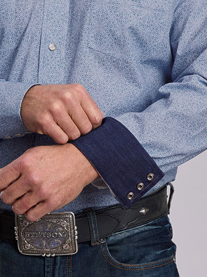 Close-up of a man's hands adjusting the cuff of a light blue patterned western shirt, paired with a black leather belt and a silver buckle. If you need any assistance with this item or the purchase of this item please call us at five six one seven four eight eight eight zero one Monday through Saturday 10:00a.m EST to 8:00 p.m EST
