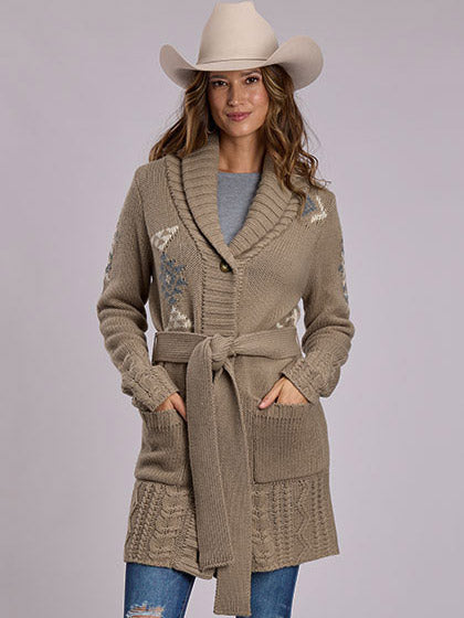 A woman wearing a beige knit shawl collar cardigan with a tie belt, decorative embroidered patterns, and front pockets, styled with a light beige cowboy hat, a gray top, and blue jeans against a solid light gray background. If you need any assistance with this item or the purchase of this item please call us at five six one seven four eight eight eight zero one Monday through Saturday 10:00a.m EST to 8:00 p.m EST