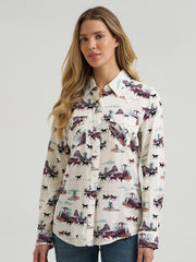 A woman modeling a long-sleeve button-up shirt with a western-themed print featuring horses, cacti, and desert landscapes on an off-white background, paired with blue jeans against a light gray studio backdrop. If you need any assistance with this item or the purchase of this item please call us at five six one seven four eight eight eight zero one Monday through Saturday 10:00a.m EST to 8:00 p.m EST