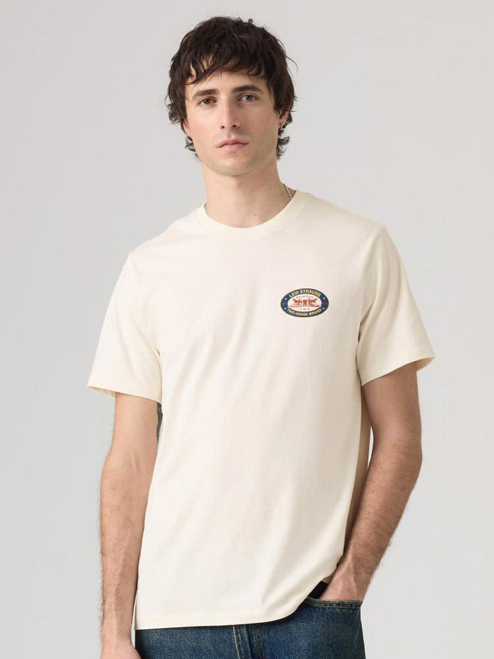 A man wearing a cream-colored Levi's t-shirt, viewed from the back. The shirt features a large graphic print with the text 'TWO HORSE BRAND' and 'LEVI STRAUSS & COMPANY' in blue, along with an orange illustration of a carriage and horses. If you need any assistance with this item or the purchase of this item please call us at five six one seven four eight eight eight zero one Monday through Saturday 10:00a.m EST to 8:00 p.m EST