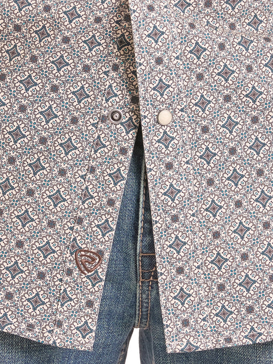Close-up of a patterned button-up shirt with a blue and brown geometric print, paired with blue jeans. The shirt features a small embroidered shield logo on the lower left front. If you need any assistance with this item or the purchase of this item please call us at five six one seven four eight eight eight zero one Monday through Saturday 10:00a.m EST to 8:00 p.m EST