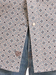 Close-up of a patterned button-up shirt with a blue and brown geometric print, paired with blue jeans. The shirt features a small embroidered shield logo on the lower left front. If you need any assistance with this item or the purchase of this item please call us at five six one seven four eight eight eight zero one Monday through Saturday 10:00a.m EST to 8:00 p.m EST