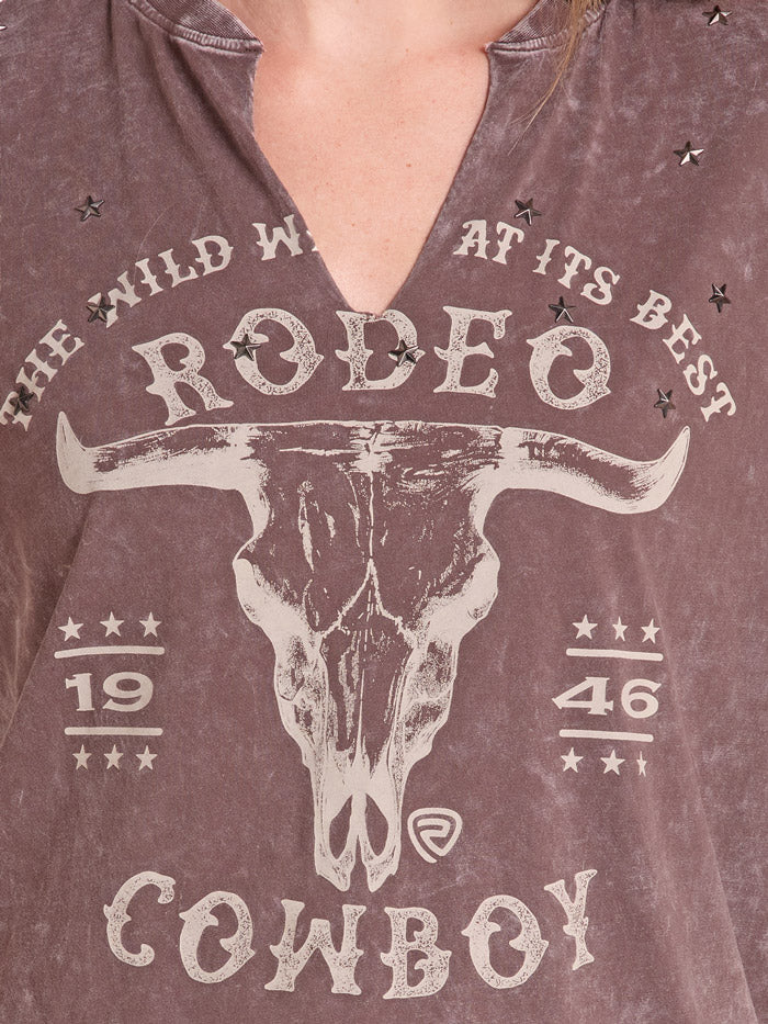 A woman wearing a brown acid-wash graphic t-shirt with a cow skull and 'Rodeo Cowboy' print, paired with a black cowboy hat and blue jeans, against a white background. If you need any assistance with this item or the purchase of this item please call us at five six one seven four eight eight eight zero one Monday through Saturday 10:00a.m EST to 8:00 p.m EST