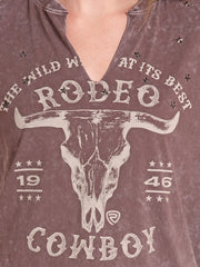 Close-up of a person wearing a distressed brown V-neck t-shirt with a western 'Rodeo Cowboy' graphic featuring a bull skull and stars. If you need any assistance with this item or the purchase of this item please call us at five six one seven four eight eight eight zero one Monday through Saturday 10:00a.m EST to 8:00 p.m EST