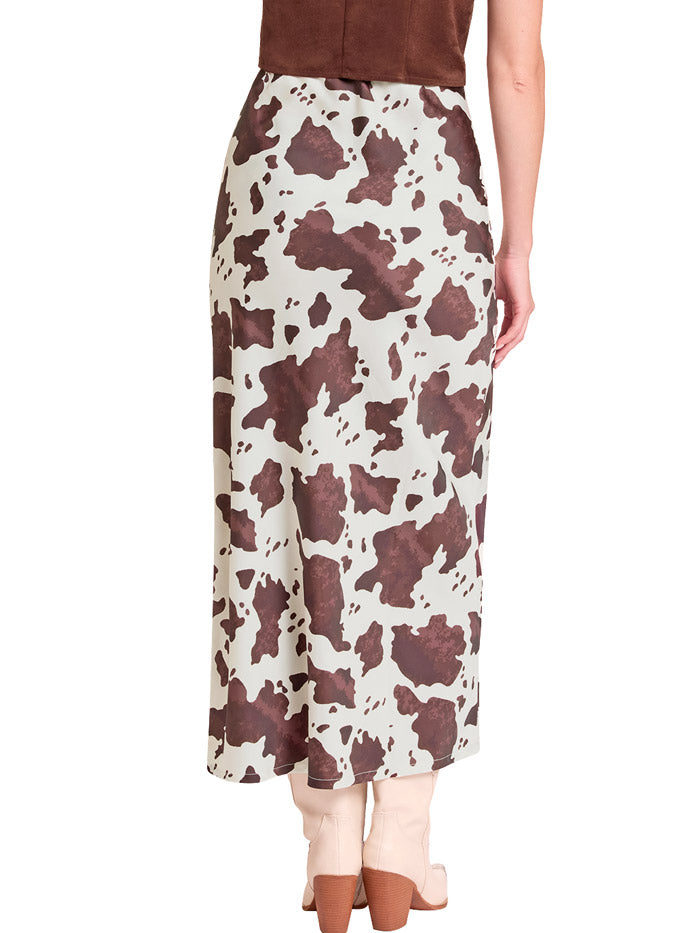 A model wearing a mid-length cow-print skirt in brown and cream, paired with light beige cowboy boots against a plain white background. If you need any assistance with this item or the purchase of this item please call us at five six one seven four eight eight eight zero one Monday through Saturday 10:00a.m EST to 8:00 p.m EST