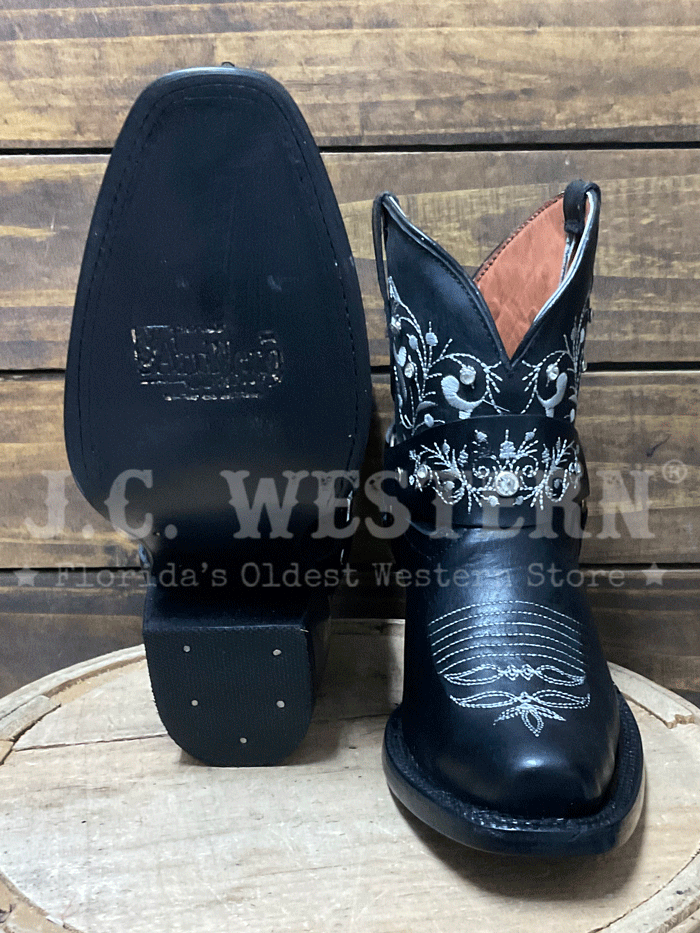 Black cowboy boots with white embroidery on a wooden barrel against a wooden background side view. If you need any assistance with this item or the purchase of this item please call us at five six one seven four eight eight eight zero one Monday through Saturday 10:00a.m EST to 8:00 p.m EST