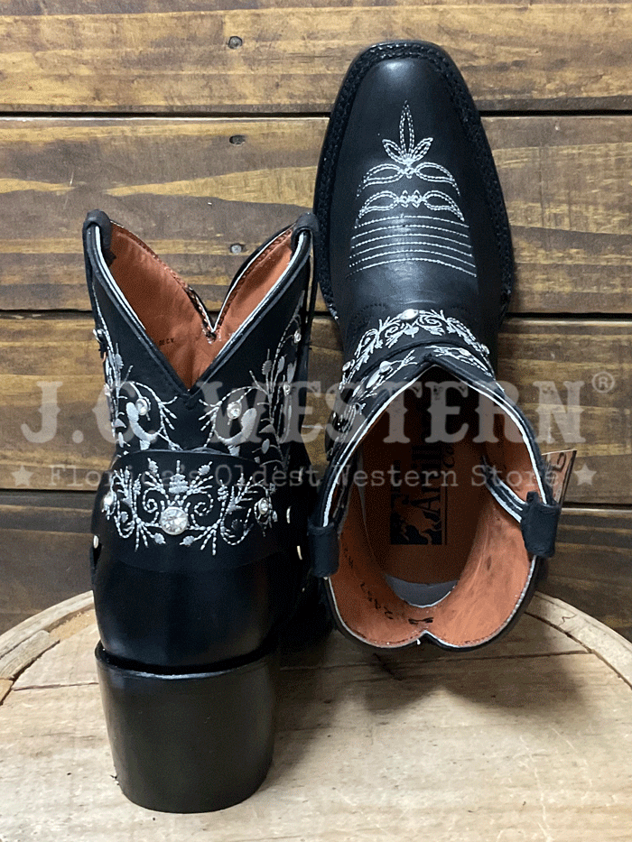Black cowboy boots with white embroidery on a wooden barrel against a wooden background side view. If you need any assistance with this item or the purchase of this item please call us at five six one seven four eight eight eight zero one Monday through Saturday 10:00a.m EST to 8:00 p.m EST