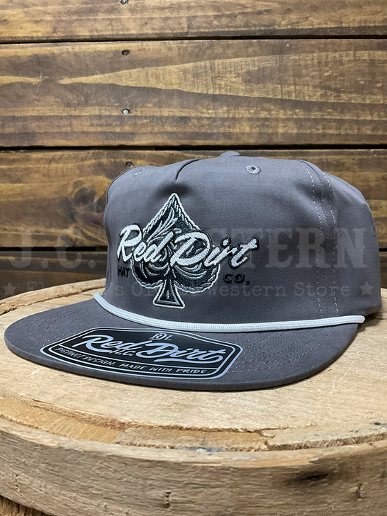 A dark gray snapback cap with a white embroidered spade logo and 'Red Dirt Co.' text on the front, resting on a rustic wooden surface against a wood plank background.If you need any assistance with this item or the purchase of this item please call us at five six one seven four eight eight eight zero one Monday through Saturday 10:00a.m EST to 8:00 p.m EST