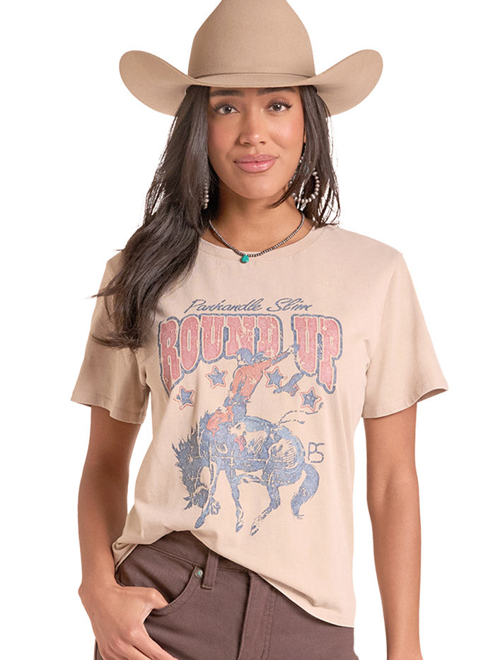 A woman wearing a beige graphic t-shirt with a western design, a matching beige cowboy hat, and brown pants, photographed against a solid white background. If you need any assistance with this item or the purchase of this item please call us at five six one seven four eight eight eight zero one Monday through Saturday 10:00a.m EST to 8:00 p.m EST