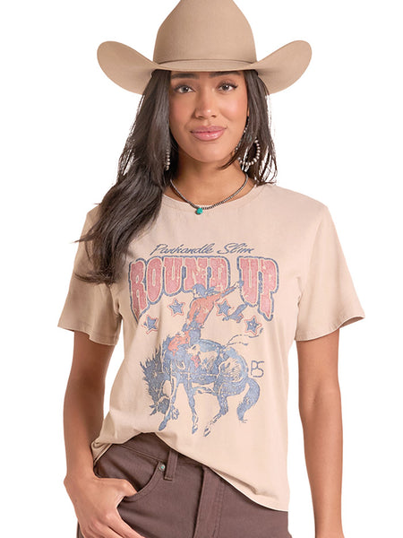 A woman wearing a beige graphic t-shirt with a western design, a matching beige cowboy hat, and brown pants, photographed against a solid white background. If you need any assistance with this item or the purchase of this item please call us at five six one seven four eight eight eight zero one Monday through Saturday 10:00a.m EST to 8:00 p.m EST