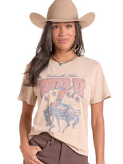 A woman wearing a beige graphic t-shirt with a western design, a matching beige cowboy hat, and brown pants, photographed against a solid white background. If you need any assistance with this item or the purchase of this item please call us at five six one seven four eight eight eight zero one Monday through Saturday 10:00a.m EST to 8:00 p.m EST