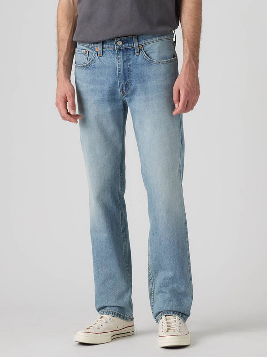 A person wearing light-wash blue jeans, a dark gray t-shirt, and white canvas sneakers, shown from the waist down against a light gray studio background. If you need any assistance with this item or the purchase of this item please call us at five six one seven four eight eight eight zero one Monday through Saturday 10:00a.m EST to 8:00 p.m EST