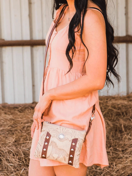 American West 9452884 Ladies Hitchin' Post Trail Rider Crossbody Hip Bag Beige on model hanging. If you need any assistance with this item or the purchase of this item please call us at five six one seven four eight eight eight zero one Monday through Saturday 10:00a.m EST to 8:00 p.m EST