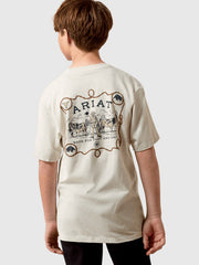 A child model shown from the back wearing a cream-colored t-shirt with a large brown graphic print on the back featuring the brand name 'Ariat' and western-themed illustrations. If you need any assistance with this item or the purchase of this item please call us at five six one seven four eight eight eight zero one Monday through Saturday 10:00a.m EST to 8:00 p.m EST