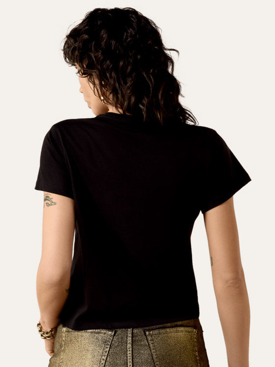 A woman modeling a black short-sleeve graphic t-shirt with a yellow and gray desert cowboy design, paired with metallic gold pants, against a plain white background. If you need any assistance with this item or the purchase of this item please call us at five six one seven four eight eight eight zero one Monday through Saturday 10:00a.m EST to 8:00 p.m EST