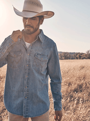 Wrangler 112361699 Mens Classic Denim Western Snap Shirt Light Wash on model outdoors. If you need any assistance with this item or the purchase of this item please call us at five six one seven four eight eight eight zero one Monday through Saturday 10:00a.m EST to 8:00 p.m EST